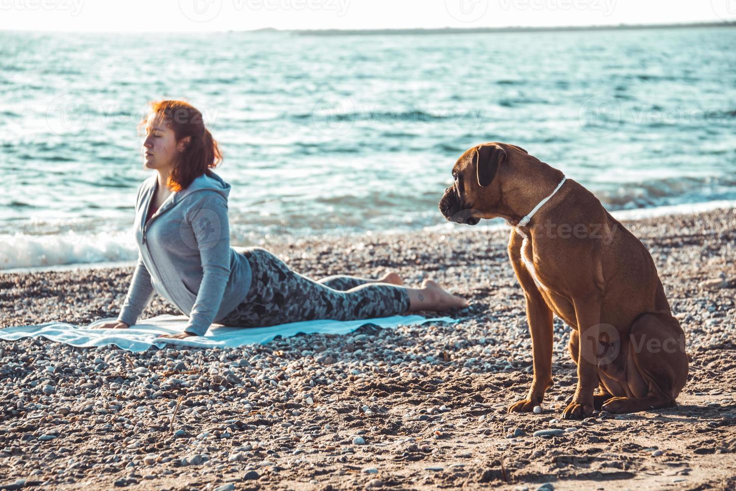 meisje doet yoga en strekt zich uit op het strand met haar hond foto