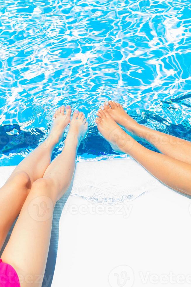 concepten zomer, ontspanning, harsen, vakantie. benen van twee meisjes die bij het zwembad zitten foto