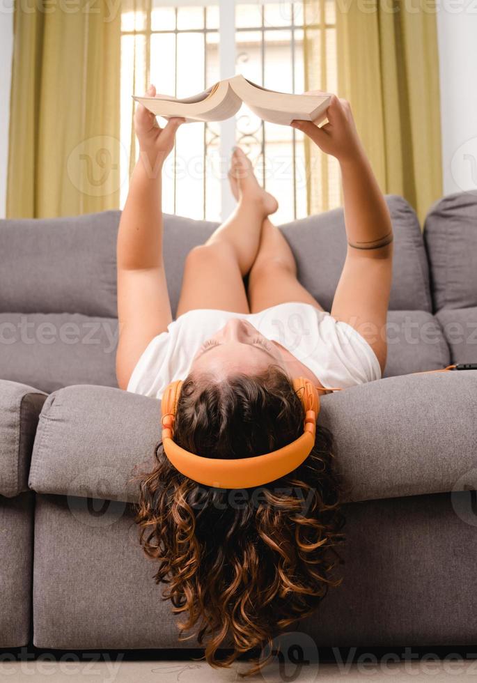 vrouw met koptelefoon lezen van een boek in de woonkamer zittend op de bank foto