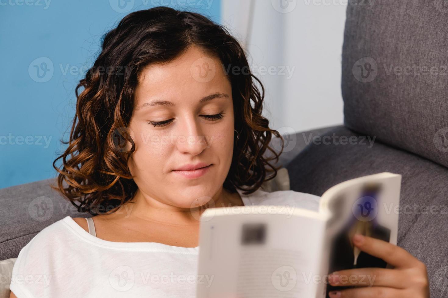 vrouw leest een boek in de woonkamer zittend op de bank foto