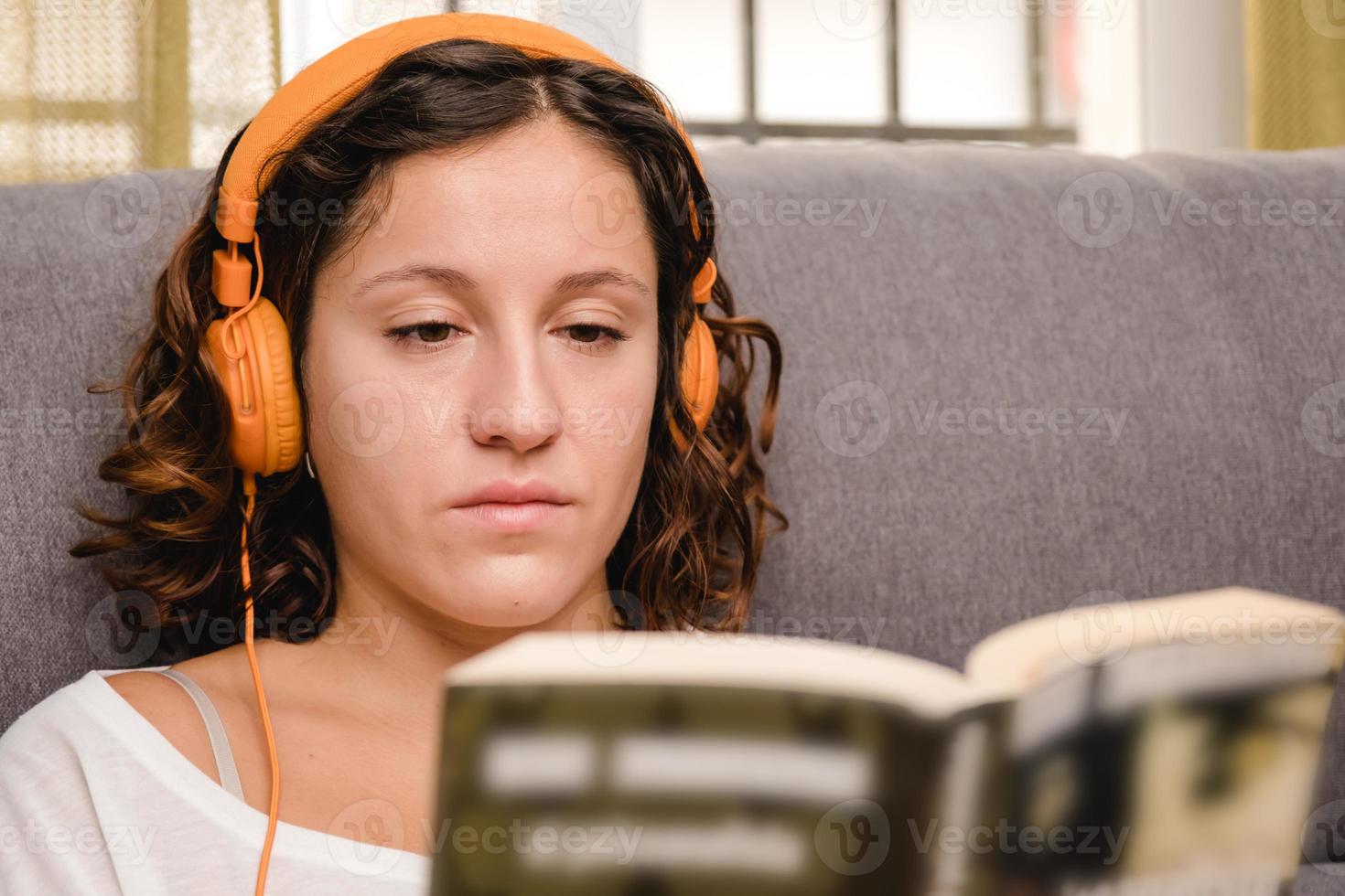 vrouw met koptelefoon lezen van een boek in de woonkamer zittend op de bank foto