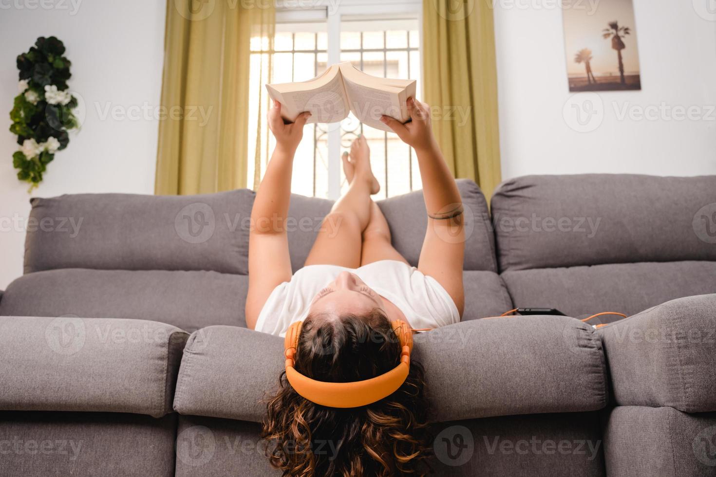 vrouw met koptelefoon lezen van een boek in de woonkamer zittend op de bank foto