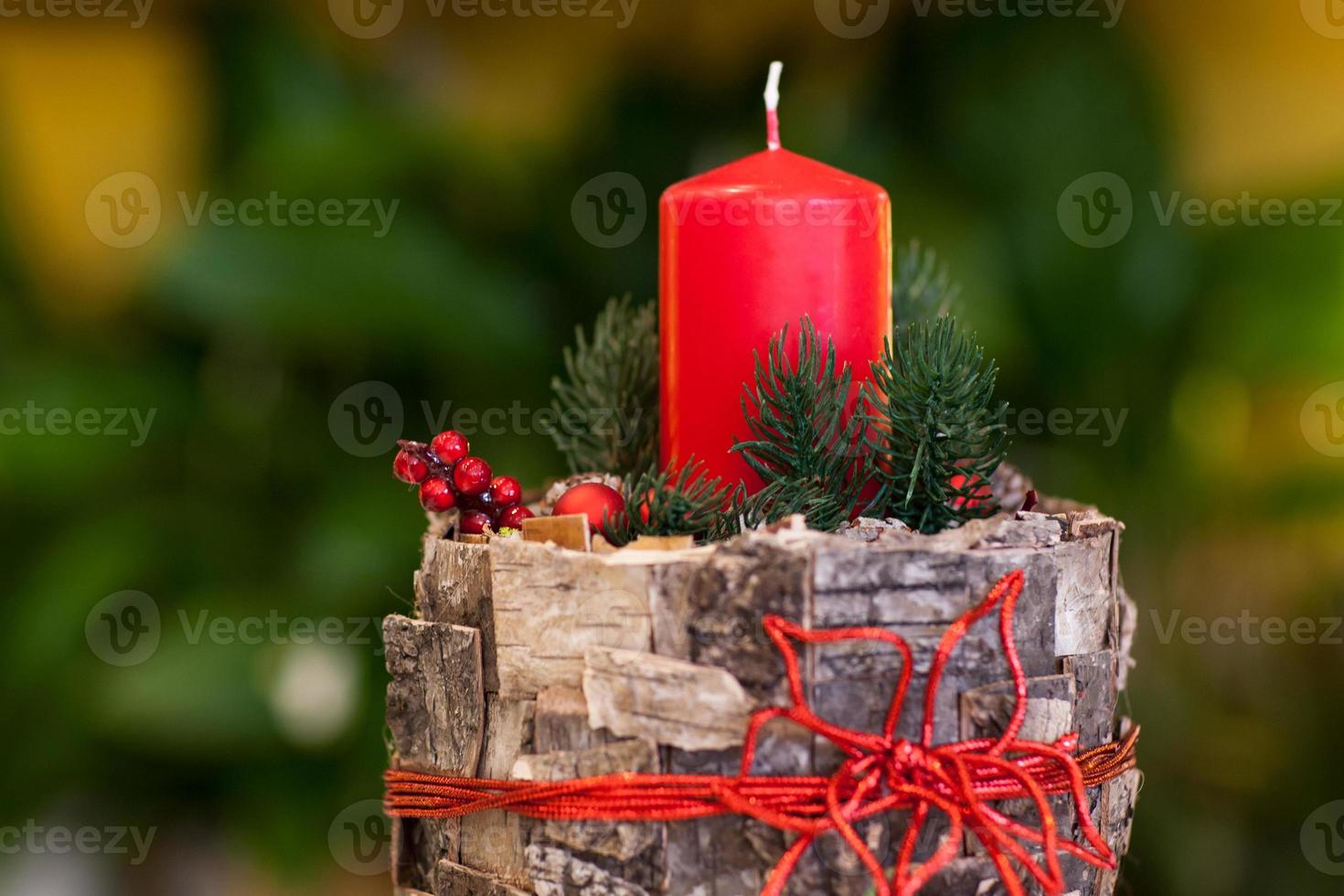 Kerstmis rode kaars op een stomp versierde boomschors en bessen en dennentakken op een wazige achtergrond close-up foto