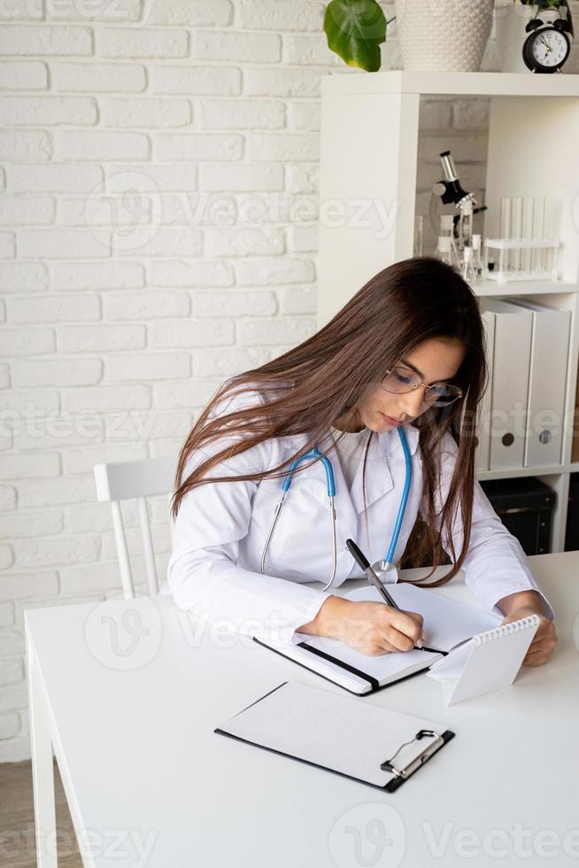 jonge doktersvrouw die in haar kabinet schrijft en medische geschiedenis of anamnese vult foto