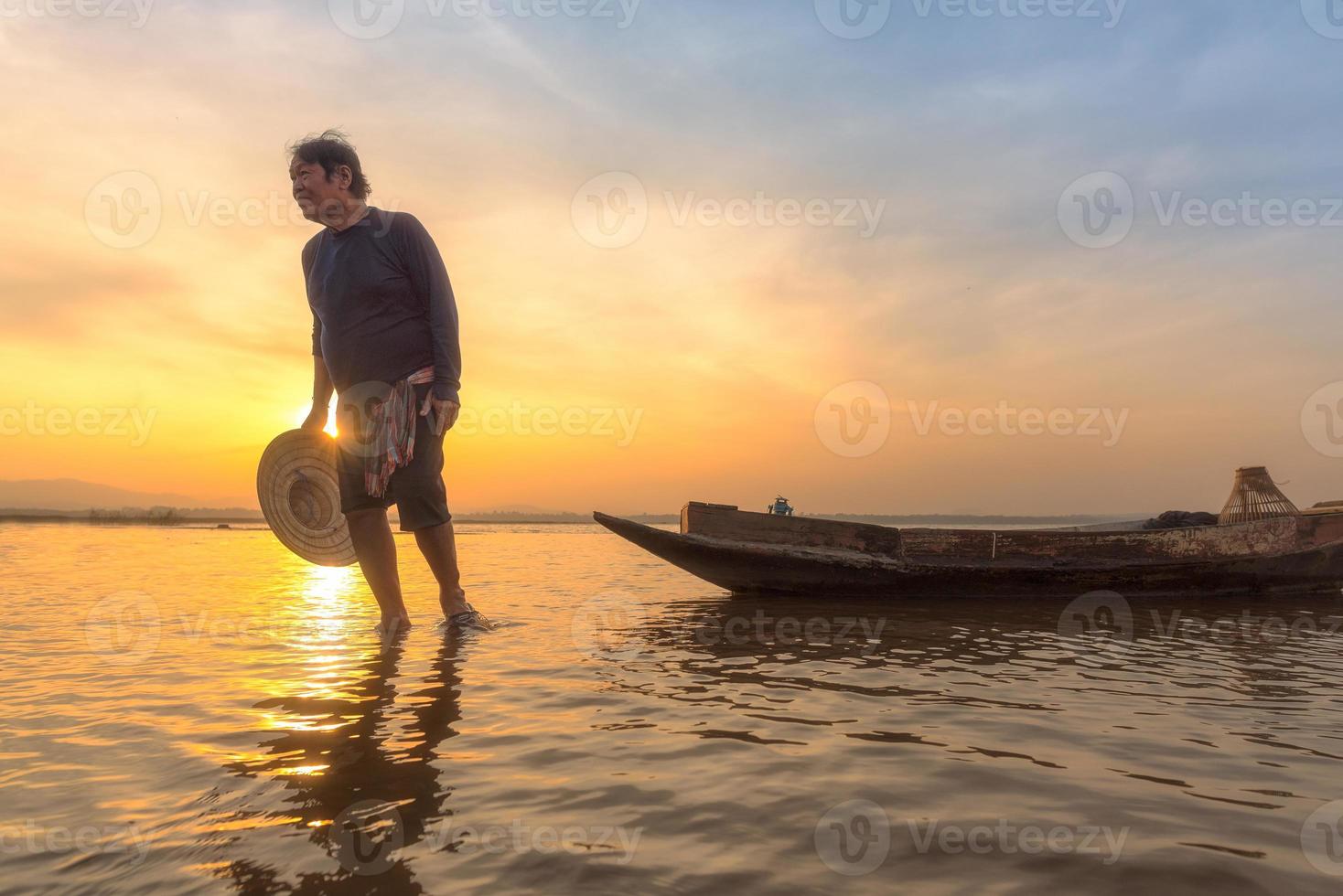 Aziatische visser met zijn houten boot die vroeg tijdens zonsopgang zoetwatervissen gaat vangen in de natuurrivier foto