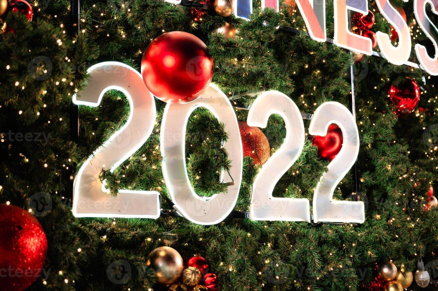 gelukkig nieuwjaar 2022 gloeien op kerstboom en ornamentballen foto