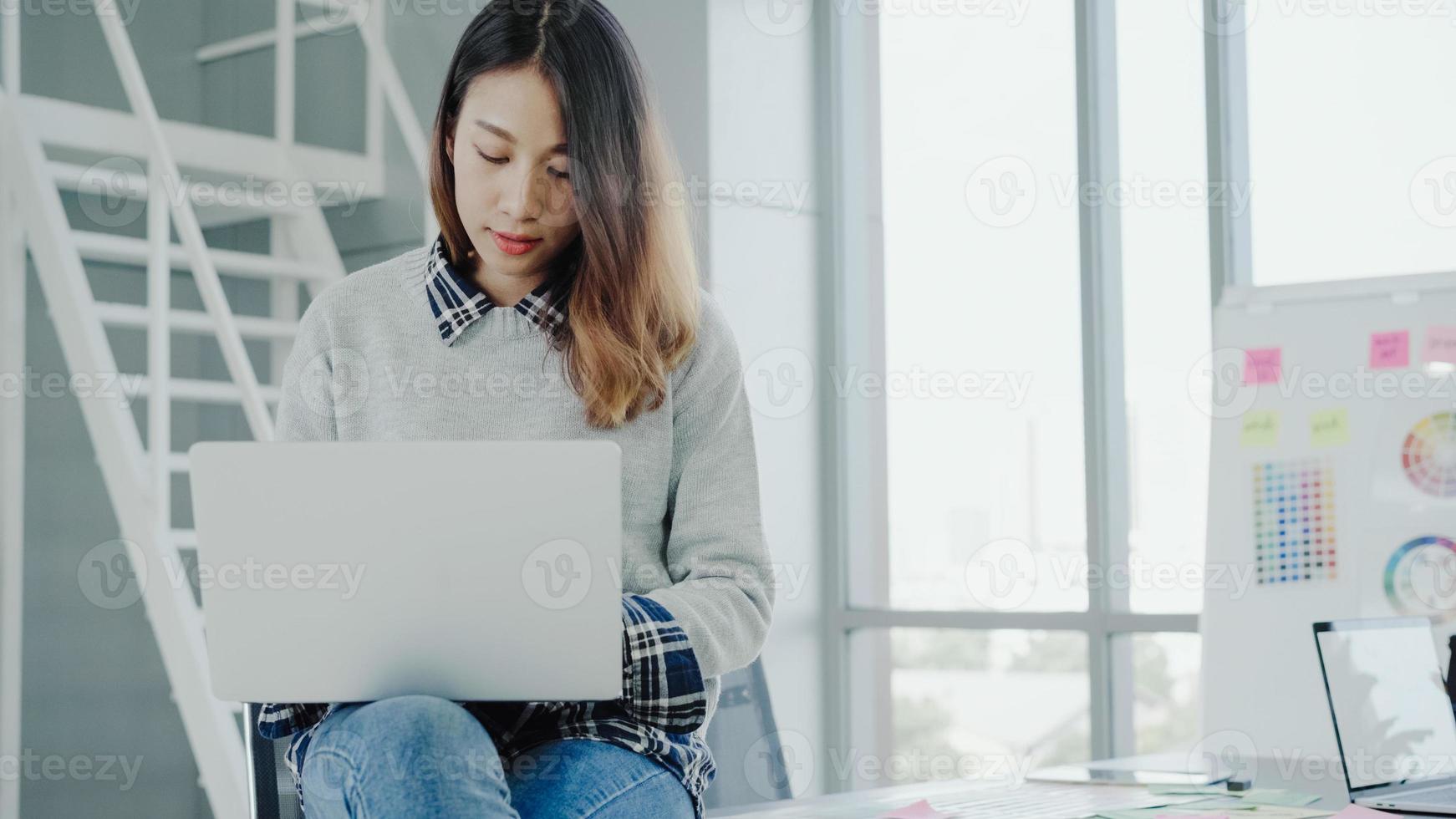 professionele Aziatische zakenvrouw die via laptop op haar kantoor werkt. jonge aziatische vrouwelijke manager die een draagbaar computerapparaat gebruikt terwijl hij op een moderne werkplek zit. foto