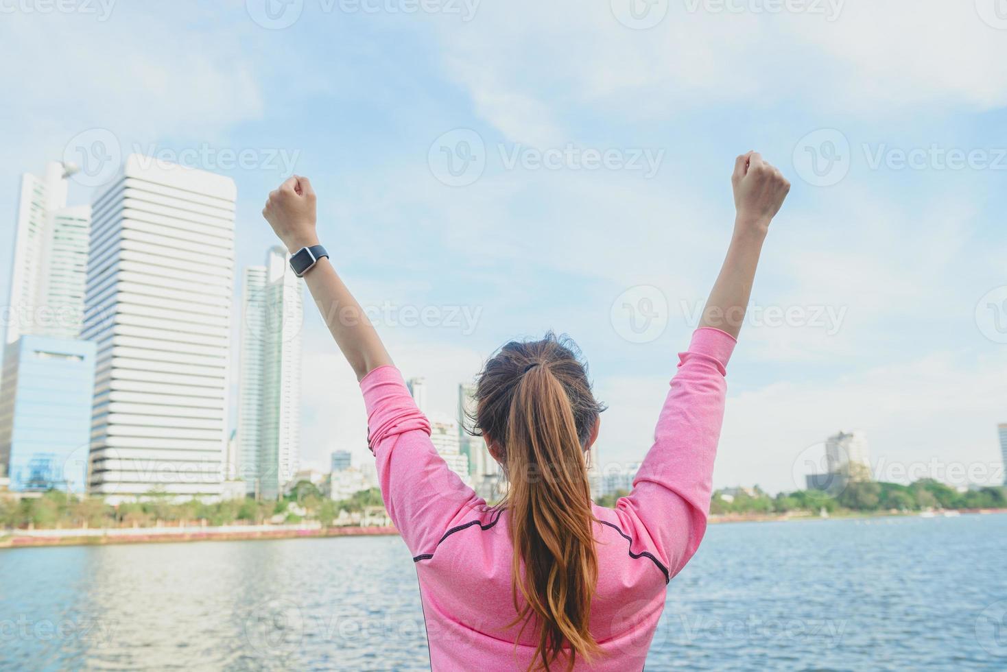 achterschot van een jonge aziatische vrouw die zich ontspant en opwarmt na een stadsoefening met een achtergrond met uitzicht op de stad en een warme, heldere lucht laat in de middag. buiten lopende oefening concept. foto