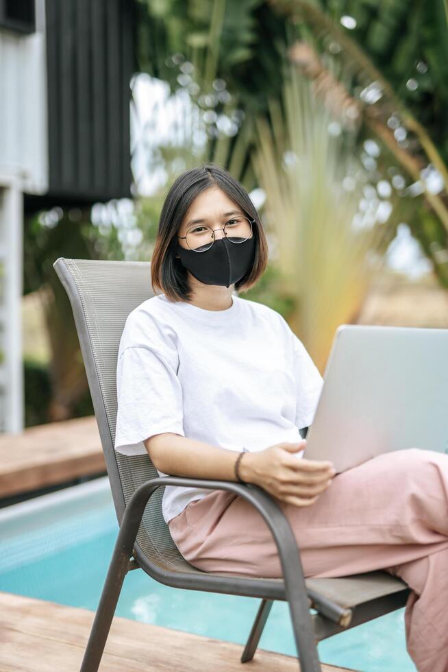 vrouwen die maskers dragen en laptops spelen bij het zwembad. foto