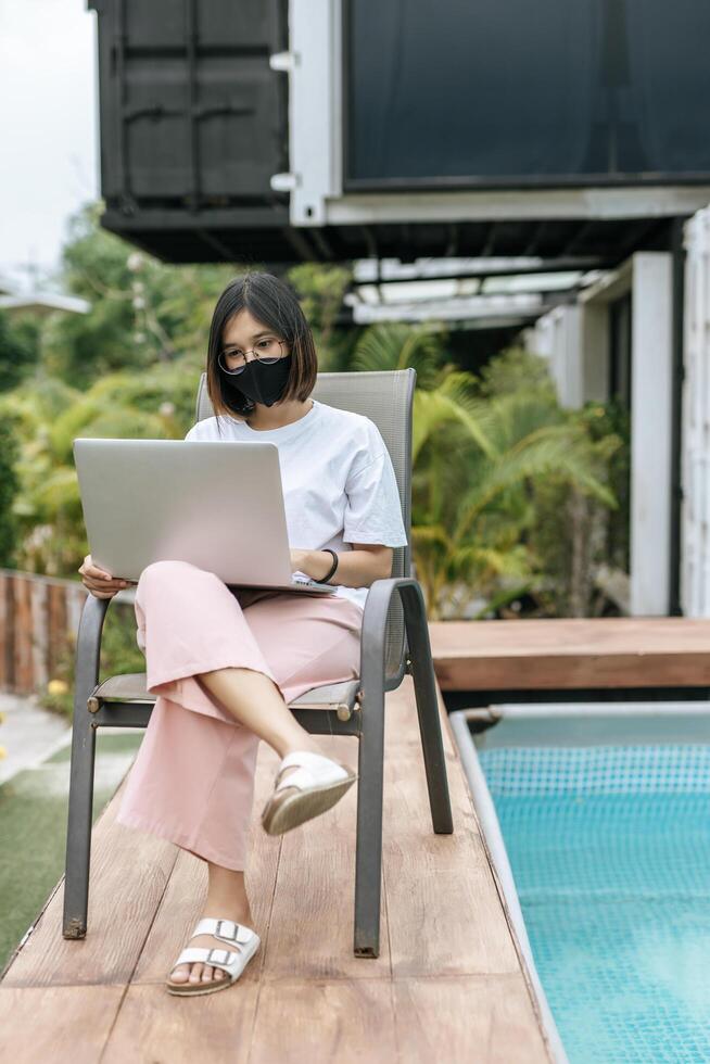 vrouwen die maskers dragen en laptops spelen bij het zwembad. foto