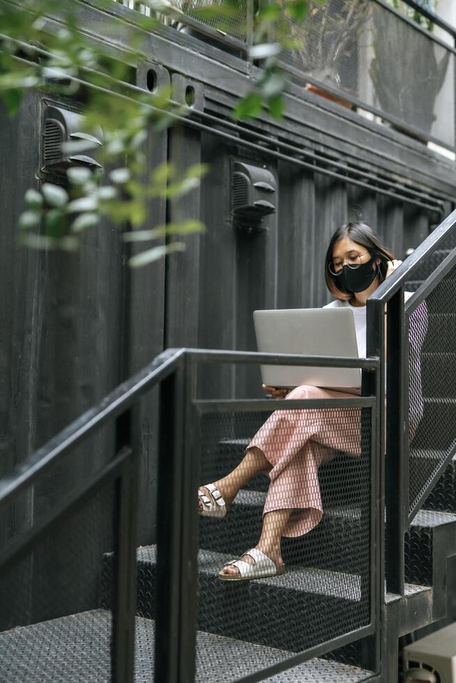 vrouwen die maskers dragen en laptops spelen op de trap. foto