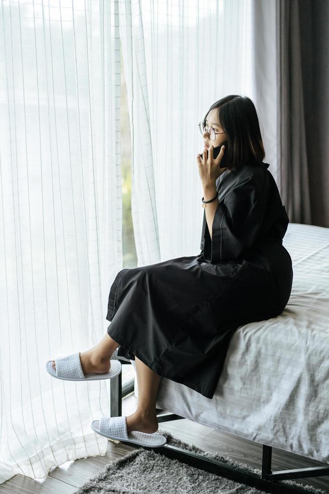 vrouw die een wit overhemd draagt, op het bed zit en aan de telefoon praat. foto