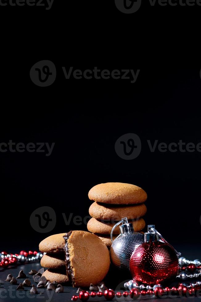 koekjes - stapel heerlijke roomkoekjes gevuld met chocoladeroom versierd met kerstversieringen op zwarte achtergrond foto