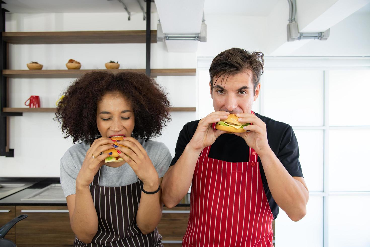 jong stel voedt terwijl ze hamburger in de keuken kookt foto