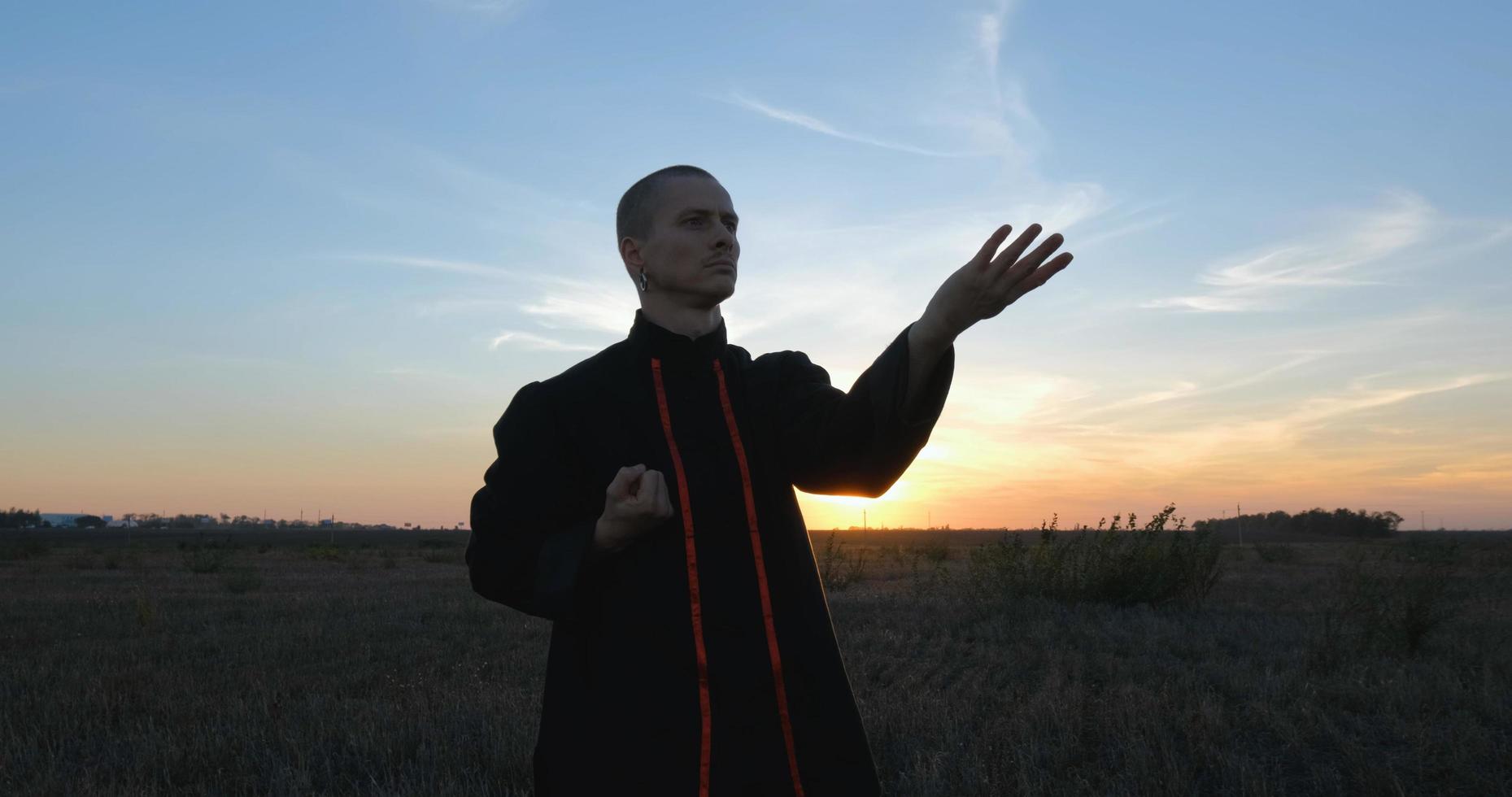 silhouet van jonge mannelijke kungfu-jager die alleen in de velden oefent tijdens zonsondergang foto