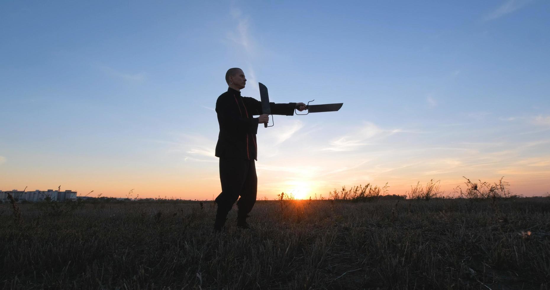 silhouet van jonge mannelijke kungfu-jager die alleen in de velden oefent tijdens zonsondergang foto