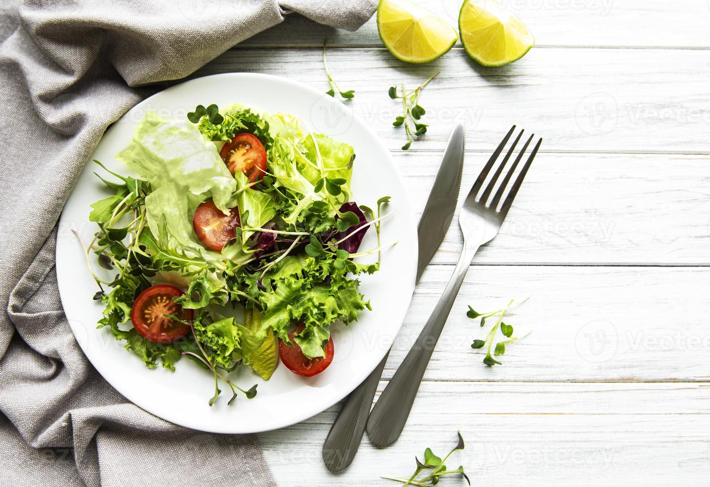 verse groene gemengde slakom met tomaten en microgreens op witte houten achtergrond. gezonde voeding, bovenaanzicht. foto