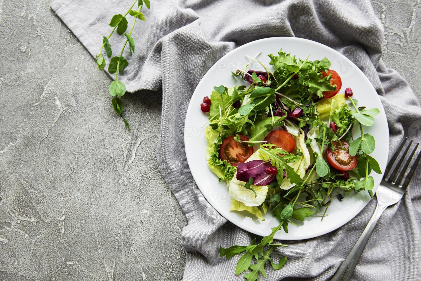 verse groene gemengde slakom met tomaten en microgreens op betonnen ondergrond. gezonde voeding, bovenaanzicht. foto