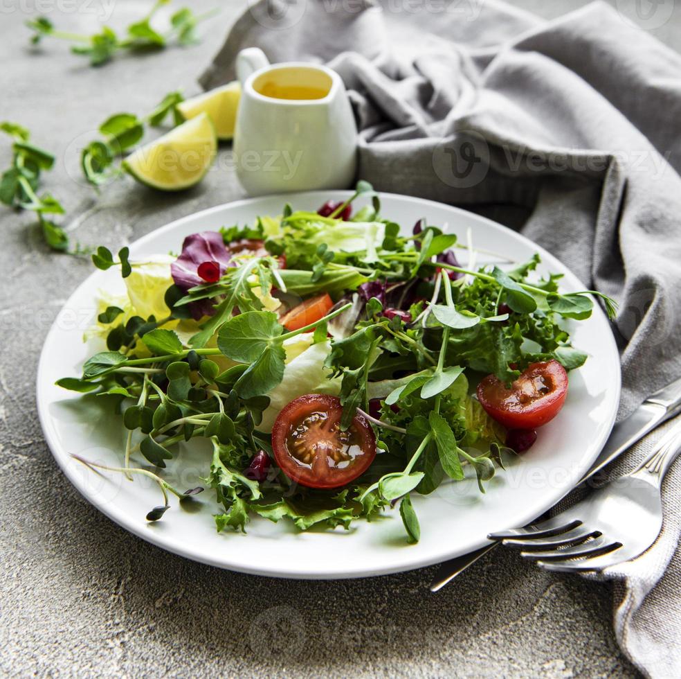 verse groene gemengde slakom met tomaten en microgreens op betonnen ondergrond. gezonde voeding, bovenaanzicht. foto