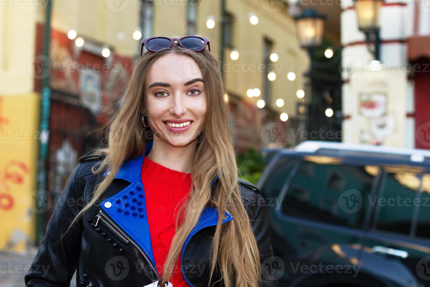 close-up mooie witte jonge vrouw met zonnebril, stijlvolle trui en leren jas poseren op straat, mooie sexy stijlvolle glimlach vrouw op stedelijke achtergrond, blanke vrouwen in de grote stad foto