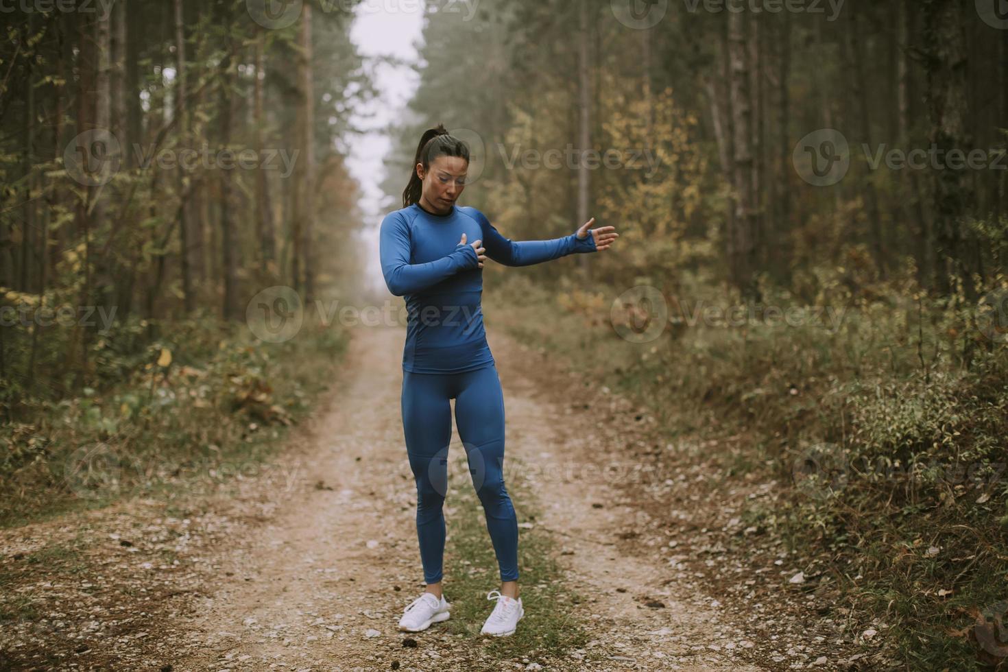 jonge vrouw in blauw trainingspak die zich uitstrekt voor de training in het herfstbos foto