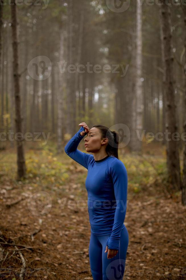 jonge vrouw neemt een pauze tijdens het sporten in de buitenlucht op het bospad in de herfst foto