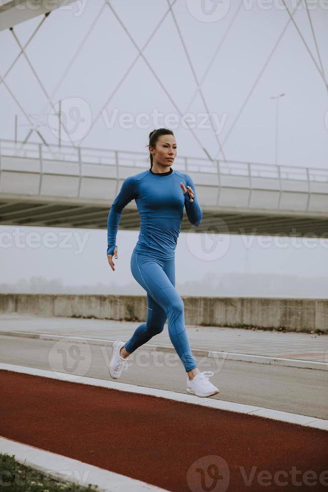 jonge vrouw in blauw trainingspak die op herfstochtend langs de rivier loopt foto