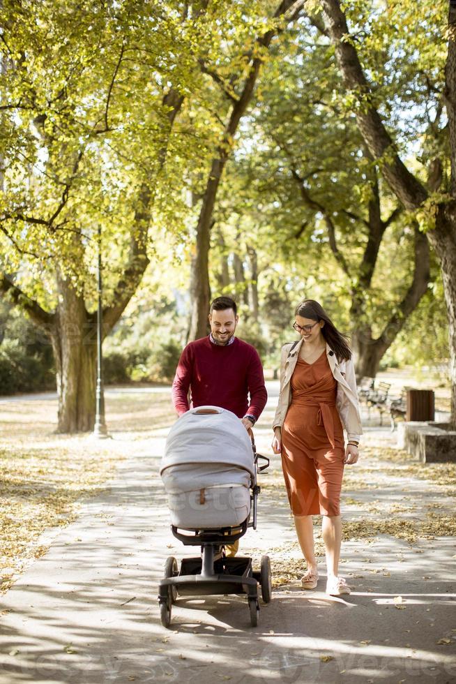 gelukkige jonge ouders die in het park wandelen en een baby in de kinderwagen besturen foto