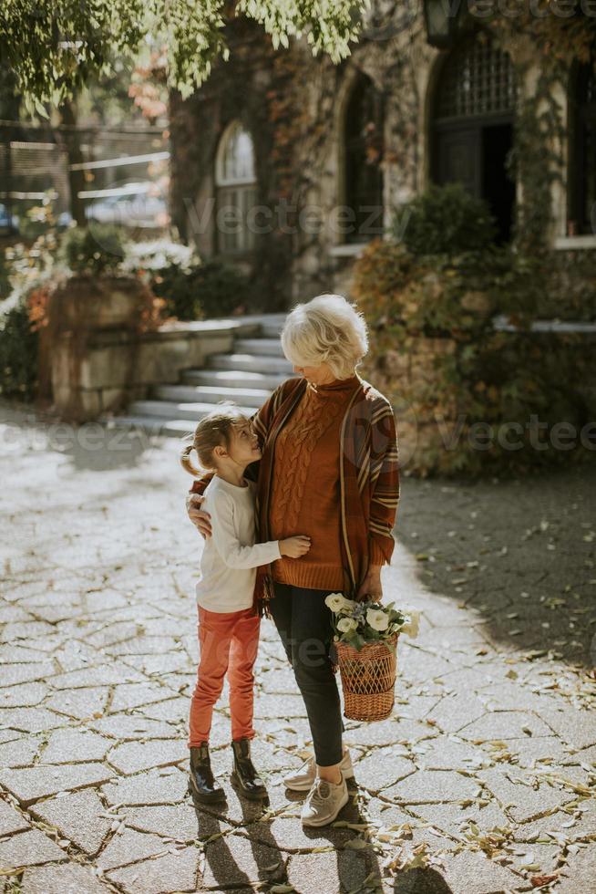 grootmoeder die plezier heeft met haar kleine kleindochter en een mand vol bloemen vasthoudt foto