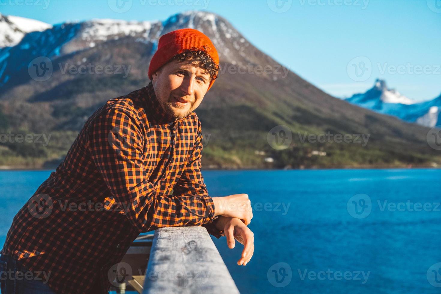 portret van een jonge man die op een houten pier staat op de achtergrond van bergen en meer. plaats voor tekst of reclame foto