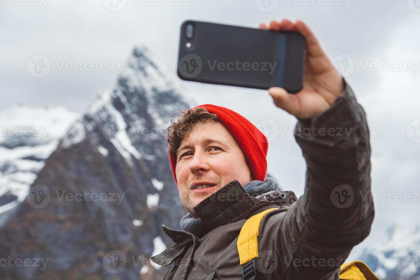 portret van een reiziger die een zelfportret maakt met een smartphone tegen de achtergrond van besneeuwde bergen en rotsen. plaats voor tekst of reclame foto