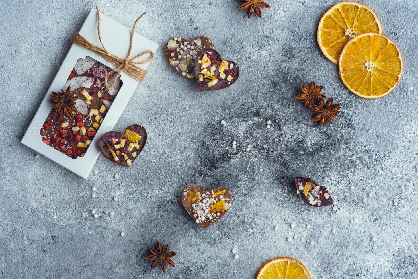 mooie compositie van handgemaakte chocolade in de vorm van grote en kleine tegels van natuurlijke ingrediënten, snoep in de vorm van hart en gedroogd fruit op een lichte textuurachtergrond. bovenaanzicht foto