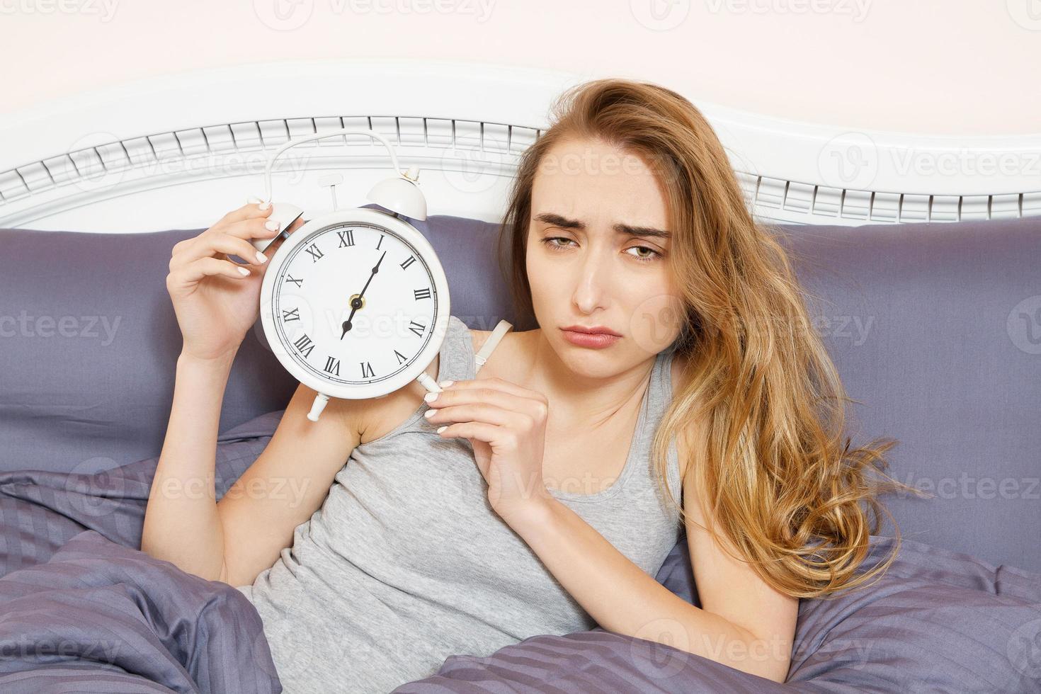 geschokte jonge vrouw wakker met alarm, verslapen werk, slechte slaap slapeloosheid. meisje houdt de klok vast als ze 's ochtends op bed ligt foto