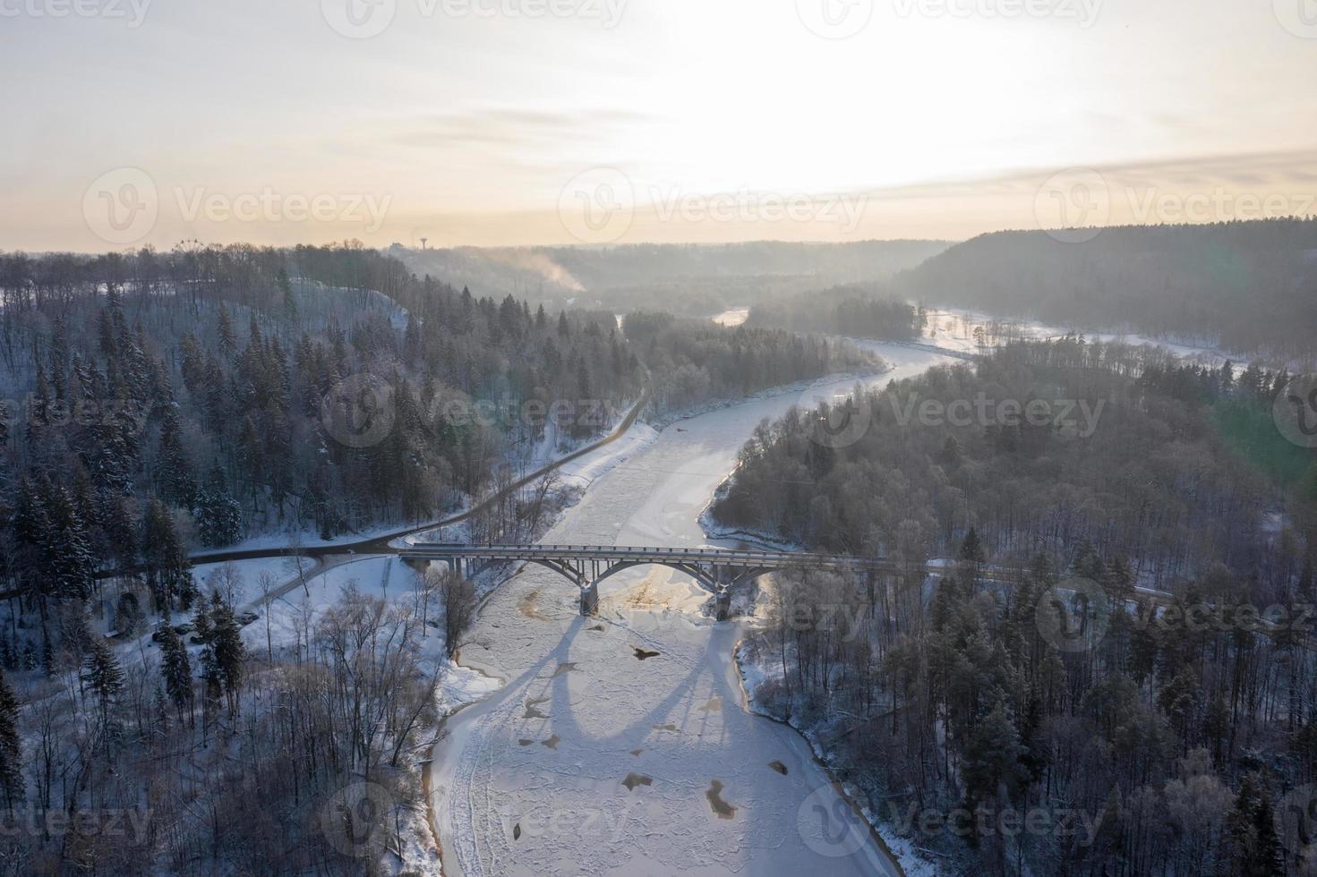 luchtfoto van de rivier en het besneeuwde bos na een sneeuwstorm in een ochtendnevel. heldere blauwe lucht. winter Wonderland. nationaal park gauja, sigulda, letland foto
