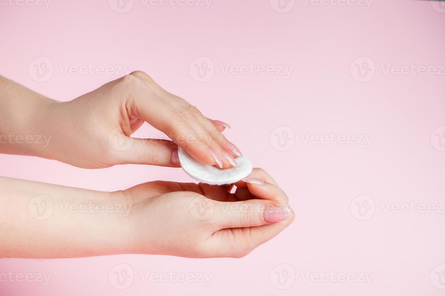 jonge vrouw verwijdert nagellak op roze achtergrond. foto