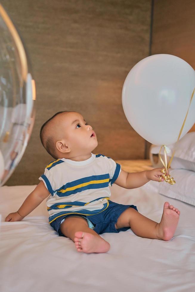 portret van een gelukkige 6 maanden oude Aziatische babyjongen die op bed zit te spelen foto