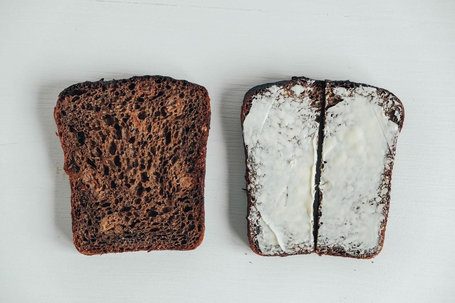 gesneden van bruin brood met boter op een witte houten achtergrond. bovenaanzicht. kopiëren, lege ruimte voor tekst foto