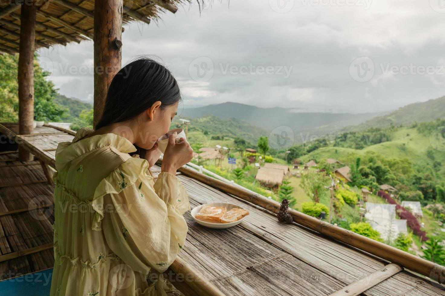 Aziatische vrouw die warme chocolademelk drinkt, toast op het balkon tussen de bergen foto