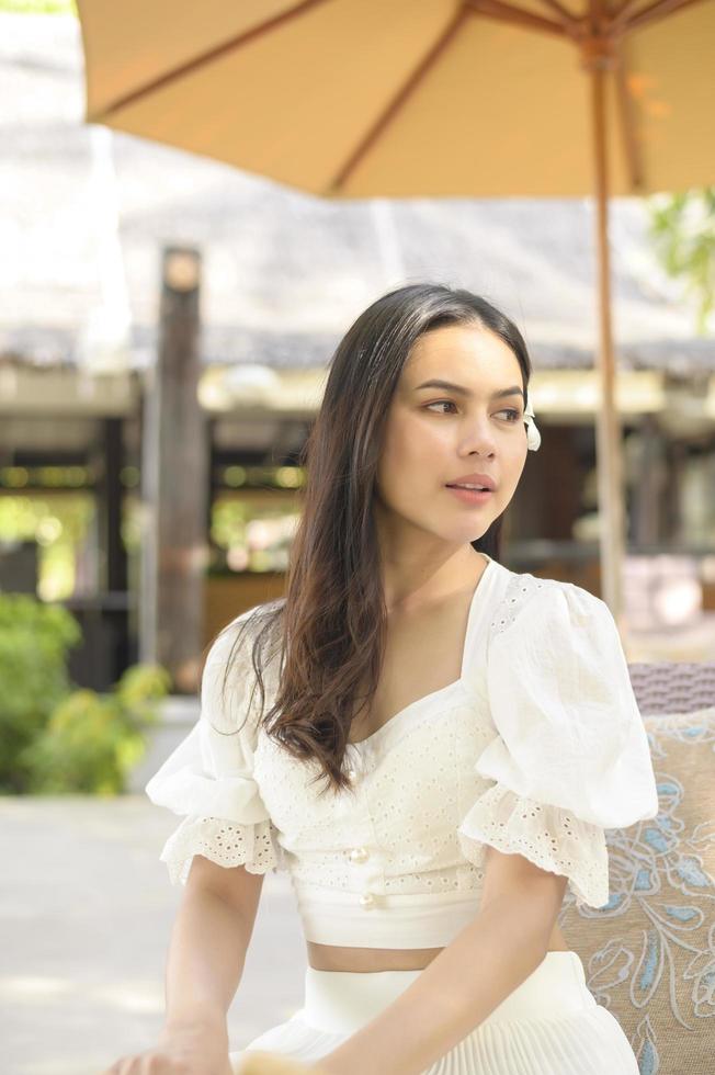 een gelukkige mooie vrouw in witte jurk die geniet en ontspant op het terras op het tropische eiland en de turquoise heldere oceaan, zomer en vakantieconcept foto