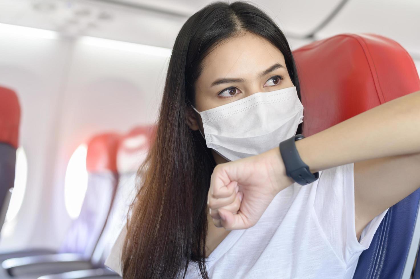 reizende vrouw met een beschermend masker aan boord in het vliegtuig met behulp van een slim horloge, reizen onder covid-19 pandemie, veiligheidsreizen, protocol voor sociale afstand, nieuw normaal reisconcept foto