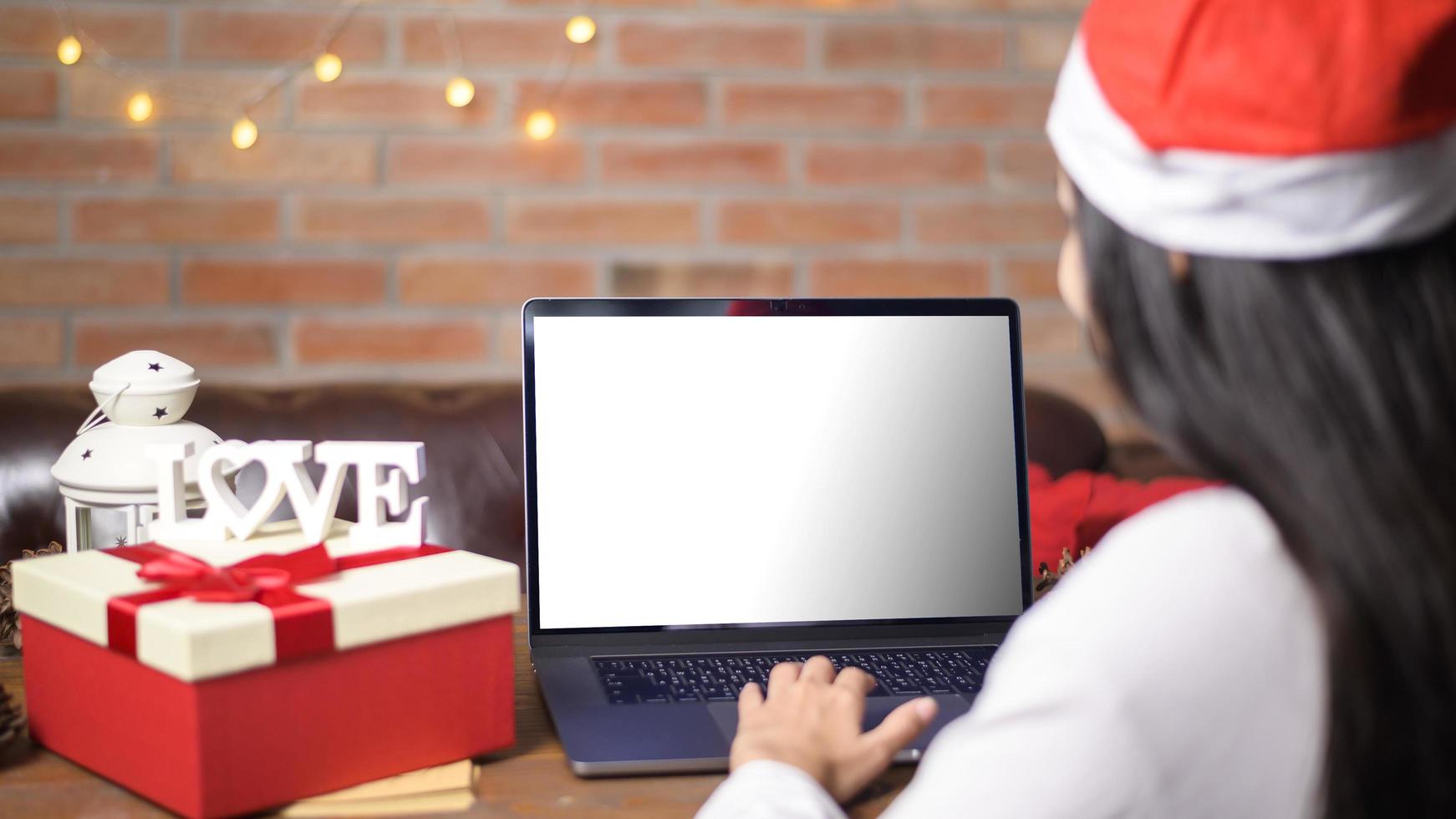 jonge lachende vrouw met rode kerstman hoed video bellen op sociaal netwerk met familie en vrienden op eerste kerstdag. laptop monitorscherm mock-up. foto