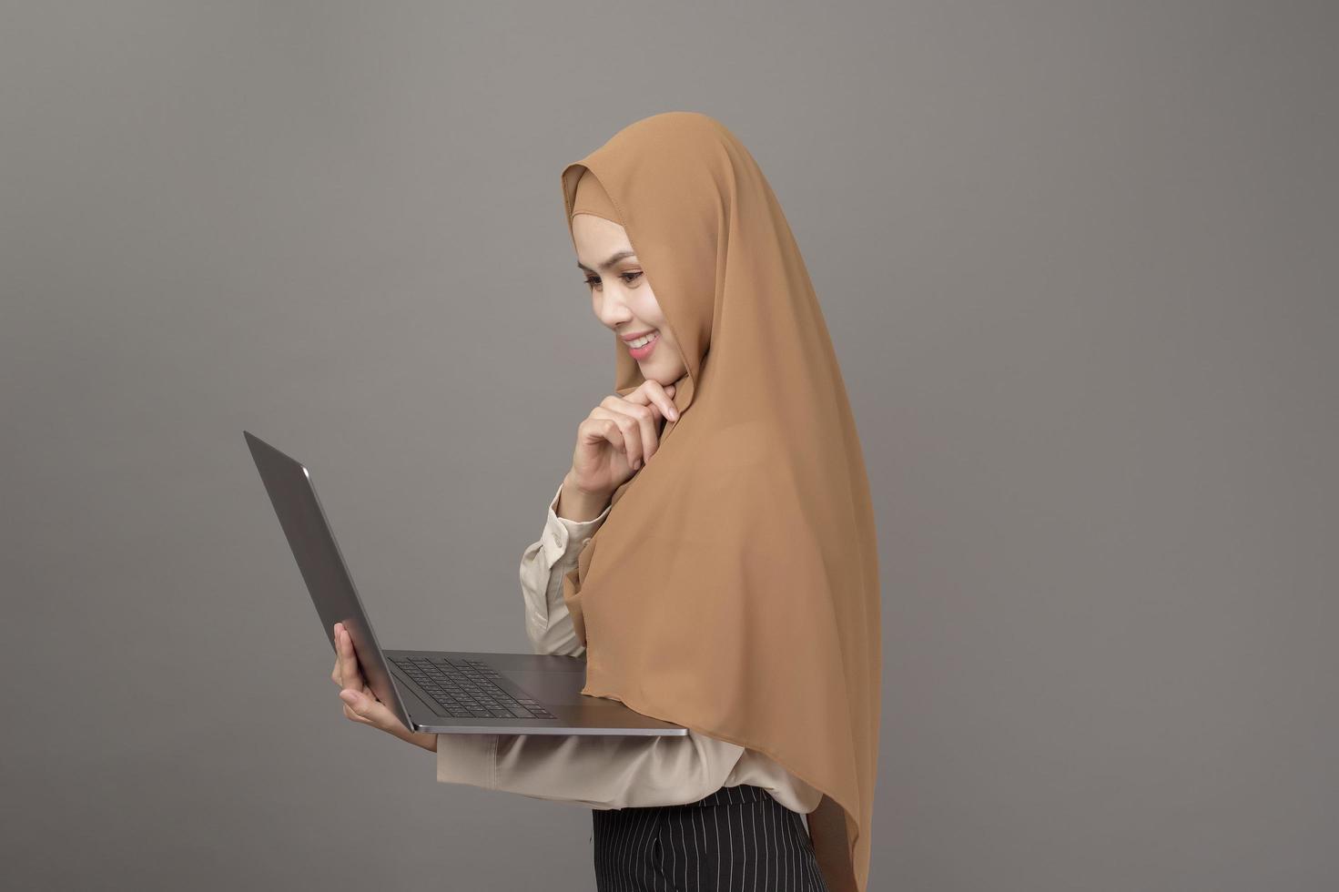 portret van mooie vrouw met hijab houdt computerlaptop op grijze achtergrond foto