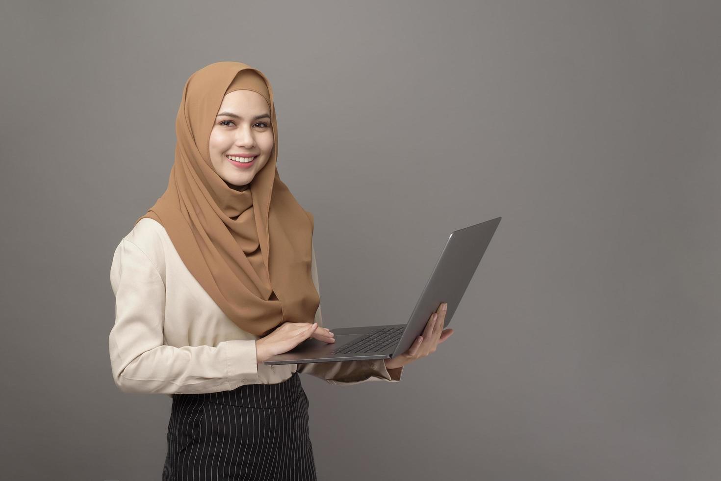 portret van mooie vrouw met hijab houdt computerlaptop op grijze achtergrond foto