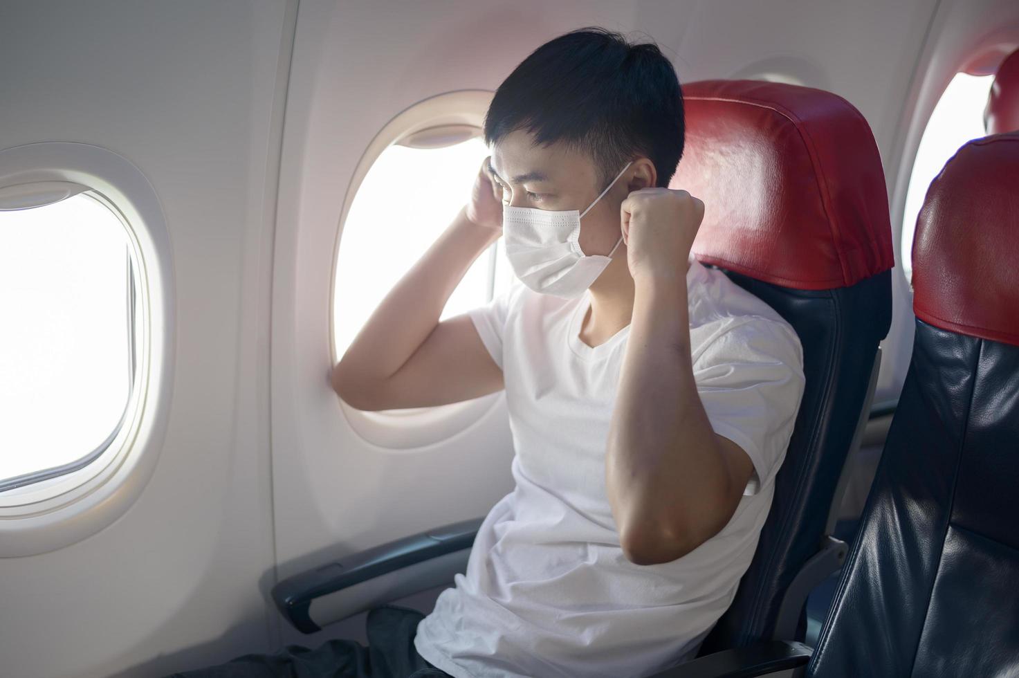 een reizende man draagt een beschermend masker aan boord van het vliegtuig, reist onder covid-19 pandemie, veiligheidsreizen, protocol voor sociale afstand, nieuw normaal reisconcept foto