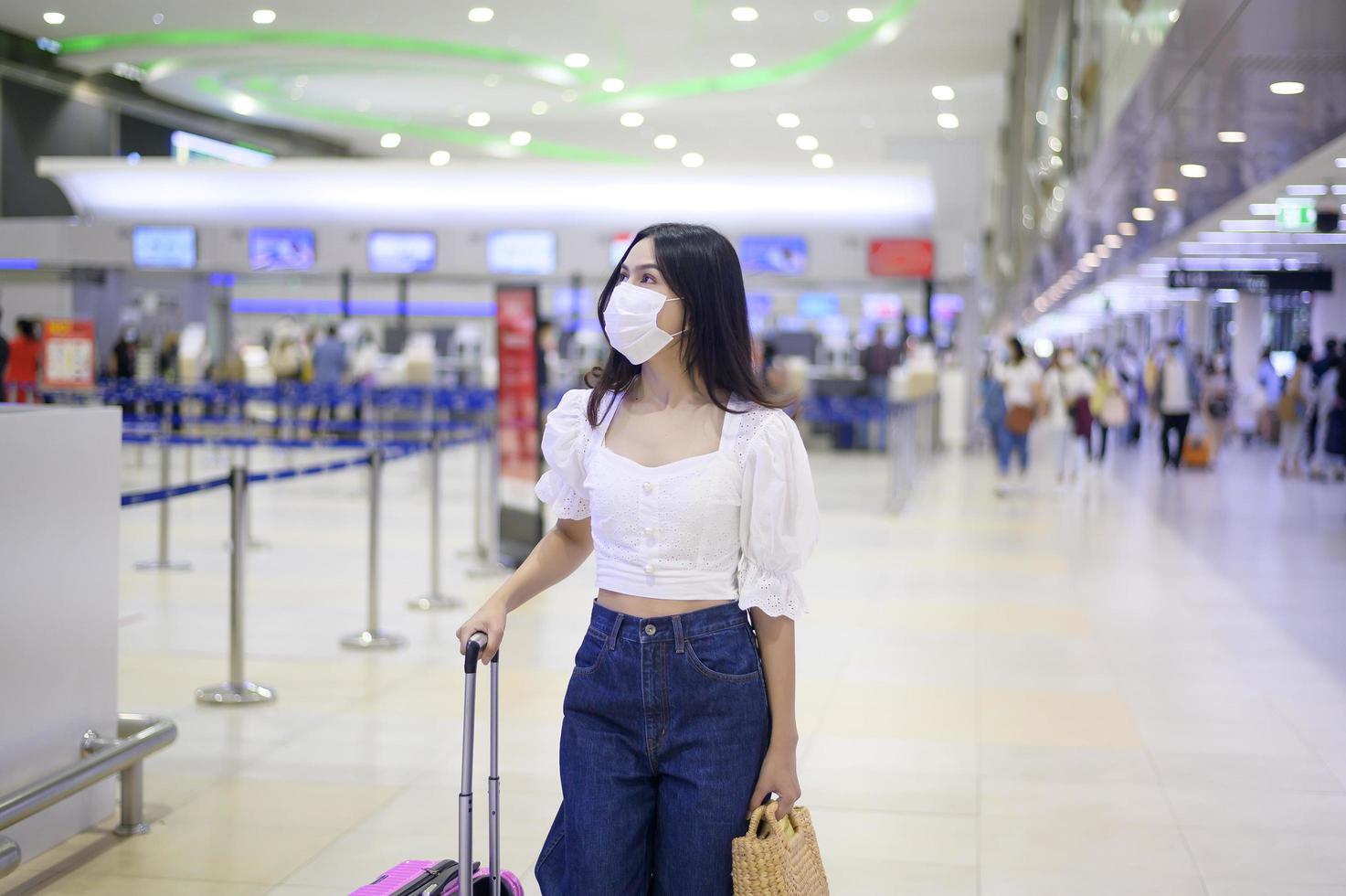 een reizigersvrouw draagt een beschermend masker op de internationale luchthaven, reist onder covid-19 pandemie, veiligheidsreizen, protocol voor sociale afstand, nieuw normaal reisconcept foto
