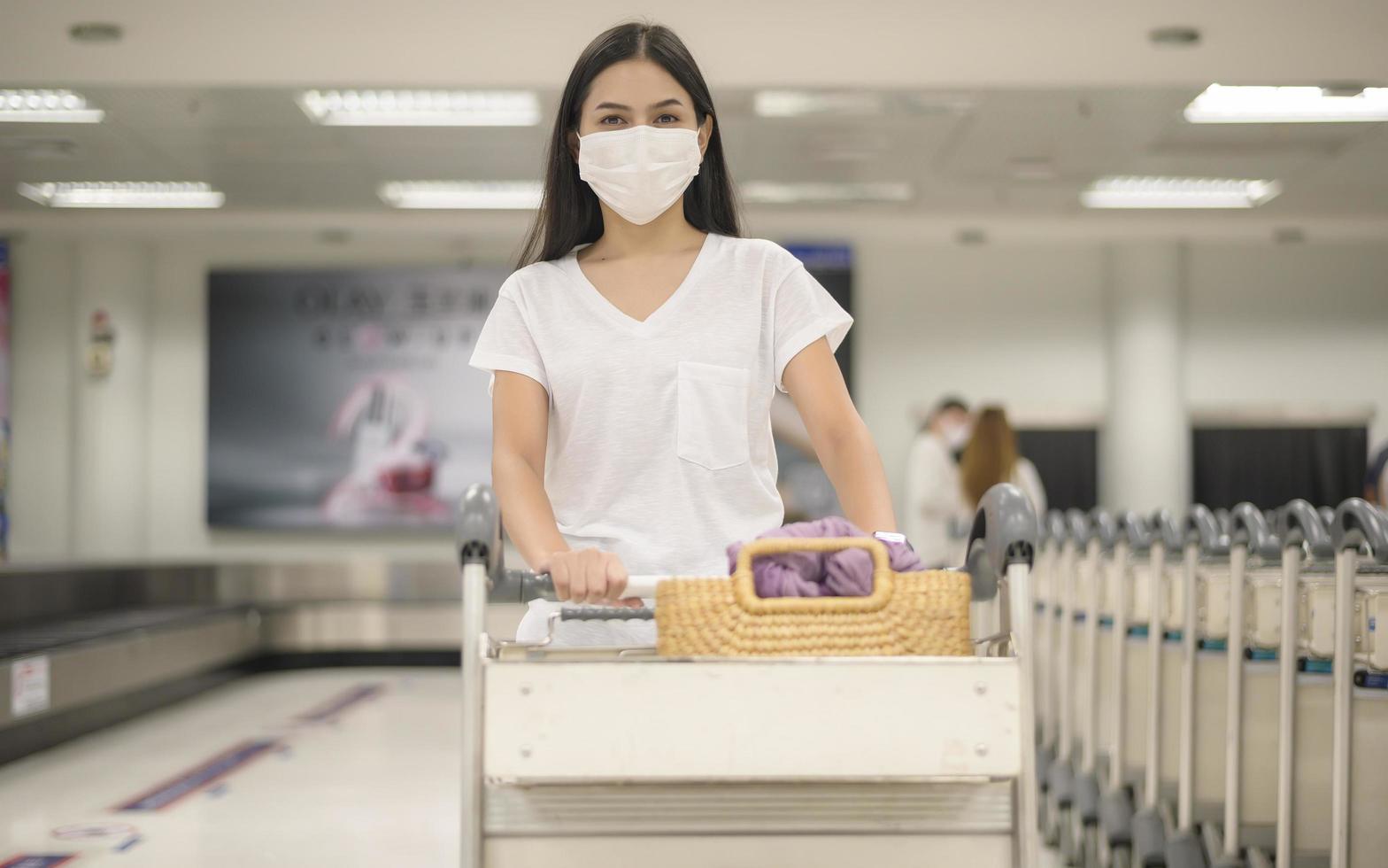 een reizende vrouw met een beschermend masker op de luchthaven met bagage op een trolley, reizen onder covid-19 pandemie, veiligheidsreizen, protocol voor sociale afstand, nieuw normaal reisconcept foto