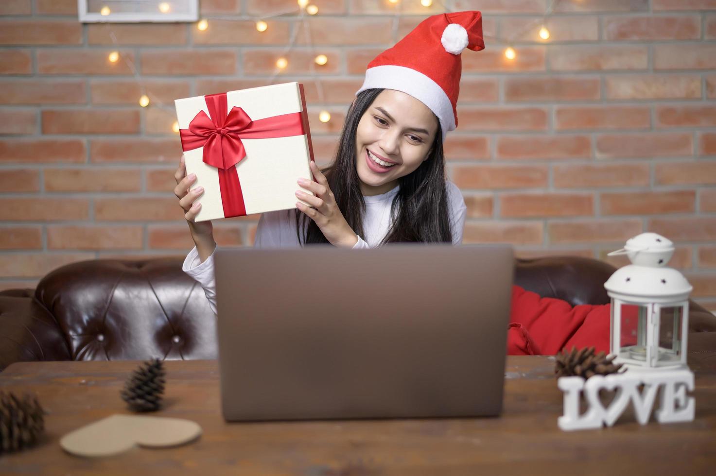 jonge lachende vrouw met rode kerstman hoed video bellen op sociaal netwerk met familie en vrienden op eerste kerstdag. foto