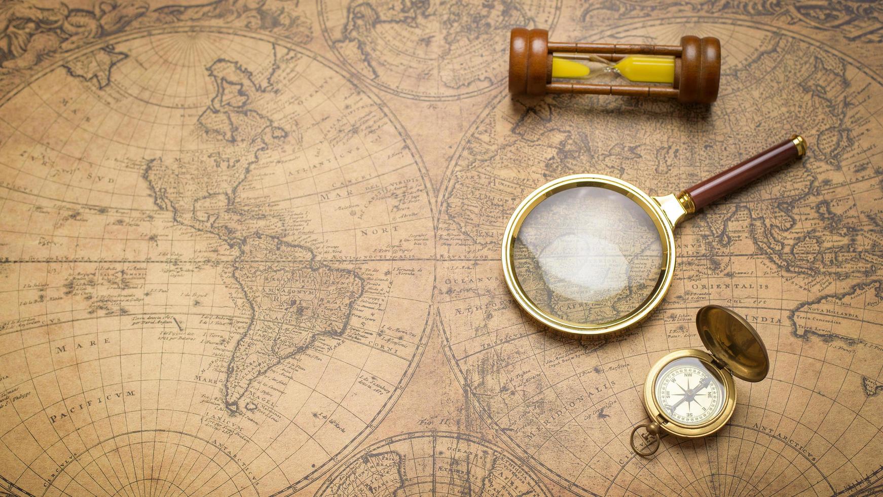 oud kompas, vergrootglas en zandklok op vintage kaart foto