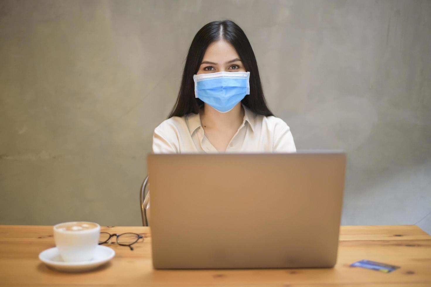 mooie vrouw met masker werkt op computerlaptop in coffeeshop foto