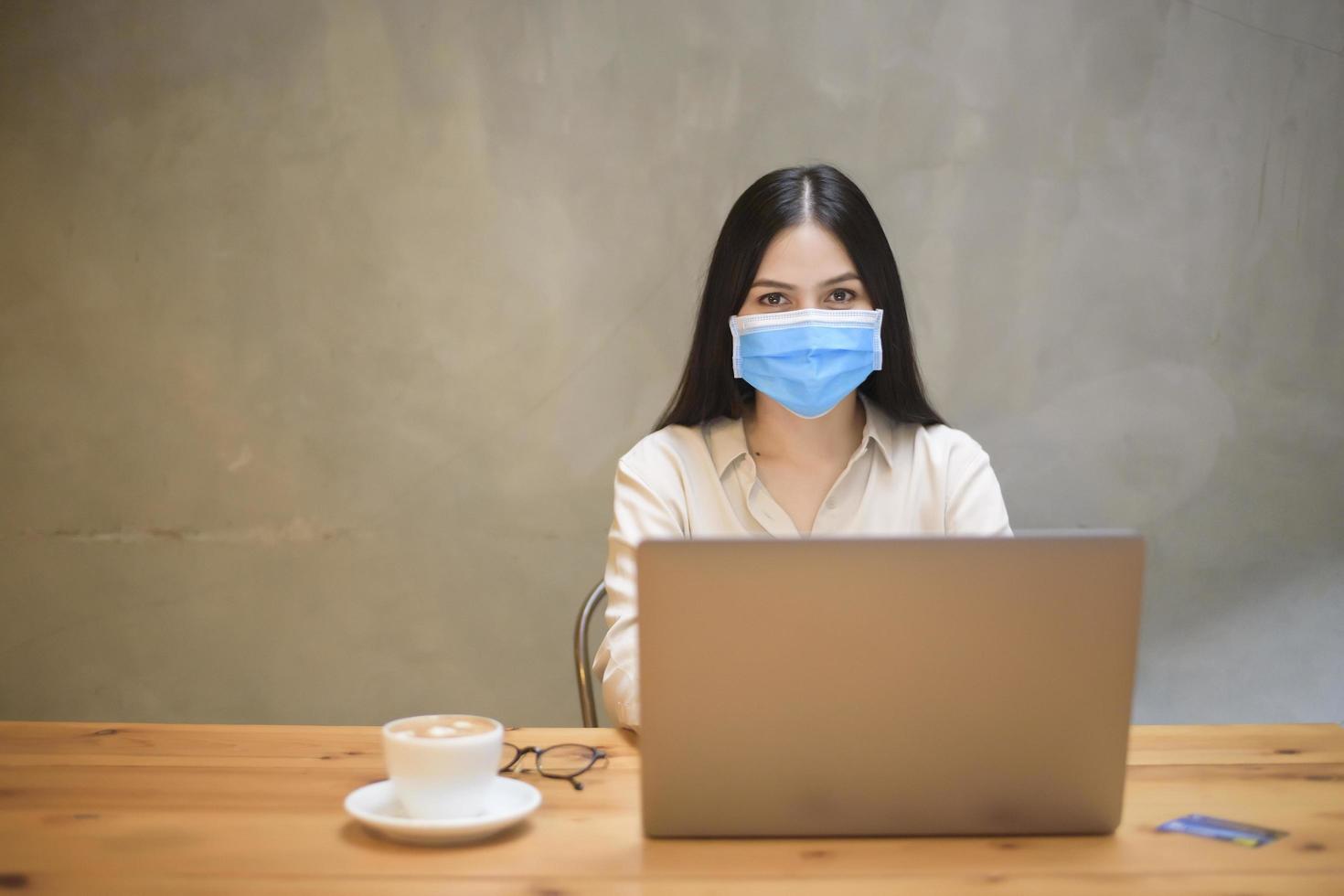 mooie vrouw met masker werkt op computerlaptop in coffeeshop foto